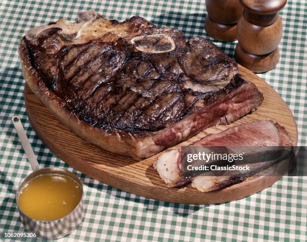 1960s HUGE PORTERHOUSE STEAK ON WOODEN PLATTER SLICED MEDIUM RARE CUP OF DRAWN BUTTER SALT PEPPER SHAKERS GREEN CHECKED CLOTH