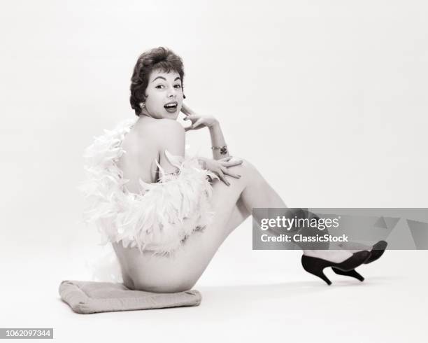 1950s NUDE WOMAN LAUGHING PLAYFUL EXPRESSION WITH FEATHER BOA DRAPED AROUND HER WEARING HEELS SITTING ON FLOOR LOOKING AT CAMERA