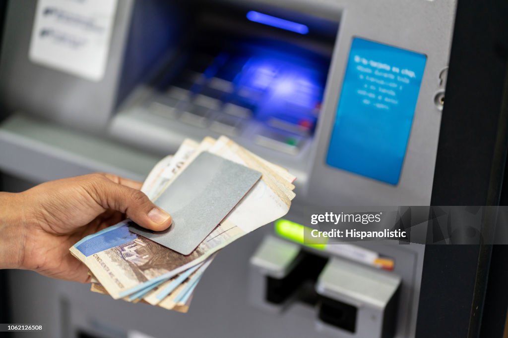 Unrecognizable man holding his debit card and cash after withdrawing from atm