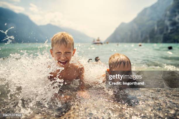 garotinhos espirrando nas ondas do lago de garda, itália - lago di garda - fotografias e filmes do acervo