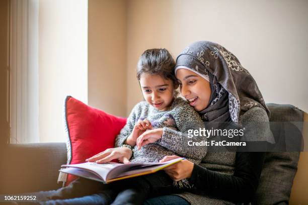 große schwester liest geschichten zu ihrer kleinen schwester - islam stock-fotos und bilder