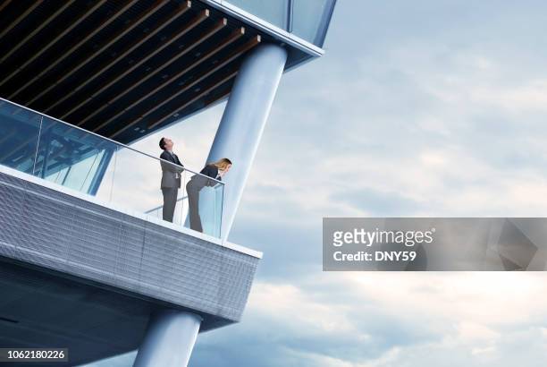 businessman and businesswoman standing on balcony of modern office building - leading edge stock pictures, royalty-free photos & images