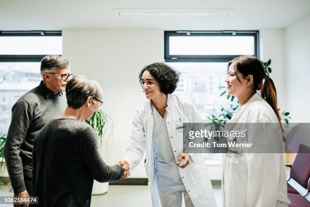 clinical doctors greeting elderly couple - female doctors group stock pictures, royalty-free photos & images