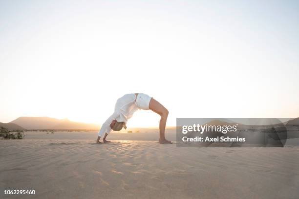 frau in yogapose rad brück auf sandigem boden - frau fotografías e imágenes de stock