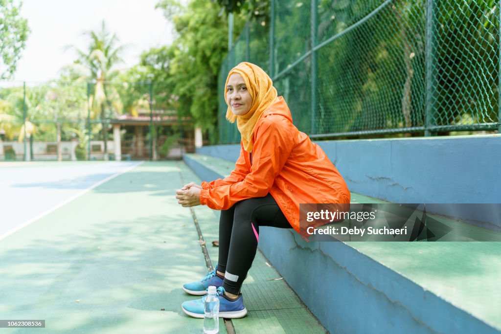 Sporty muslim woman wearing bright color cloths resting and sitting on the bench at the sport park