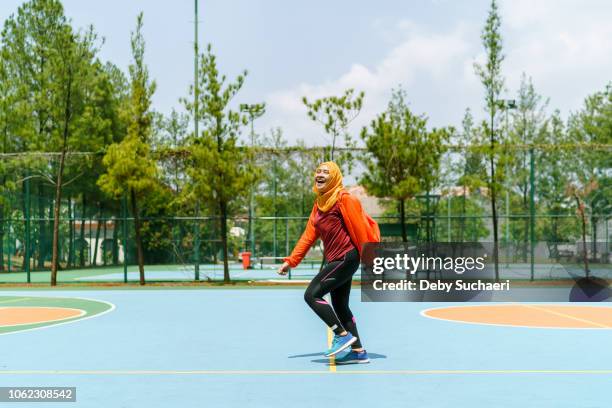 sporty muslim woman and runner wearing bright color cloths confidently laughing and walking in a basketball park bright color cloths confidently laughing and walking in a basketball park - malay hijab stock-fotos und bilder