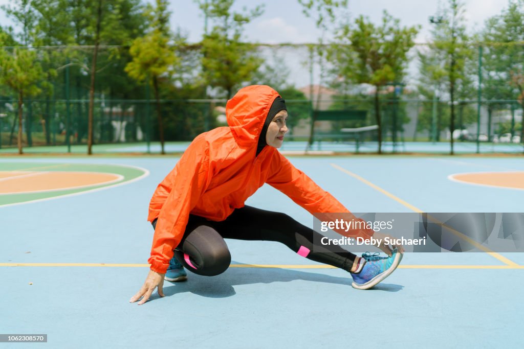 Sporty muslim woman and runner with hijab stretching legs in the park