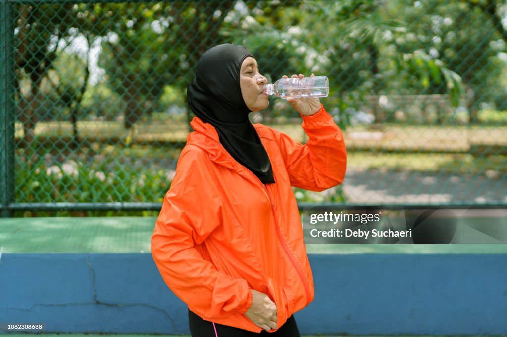 Proud and confident muslim woman with hijab drinking mineral water after sport in the park