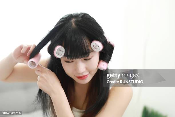 young woman putting curlers in hair - hair curlers stockfoto's en -beelden