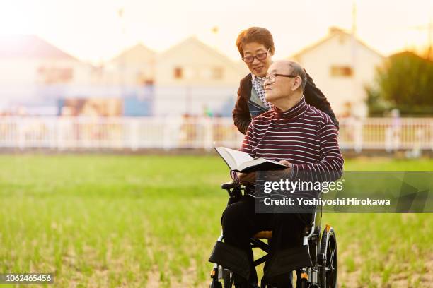 smiling wife assisted living with wheelchair,man has book on his hand - 介護施設 ストックフォトと画像