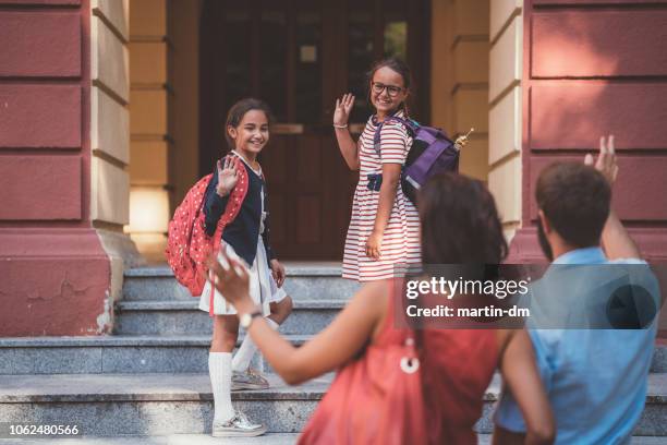 escolares saludando con la mano a sus padres antes de entrar en el edificio de la escuela - first day of school fotografías e imágenes de stock