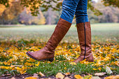 Woman wearing brown leather boot and walking in fallen leaves.