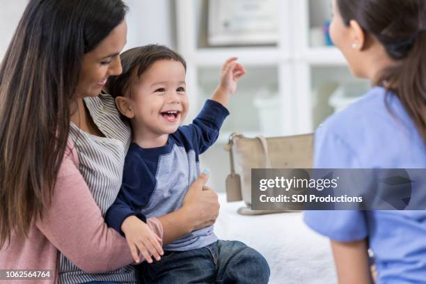 cheerful toddler boy smiles at pediatrician - child and doctor stock pictures, royalty-free photos & images