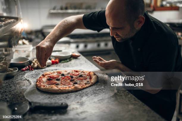 putting seasoning on pizza - pizzeria stock pictures, royalty-free photos & images