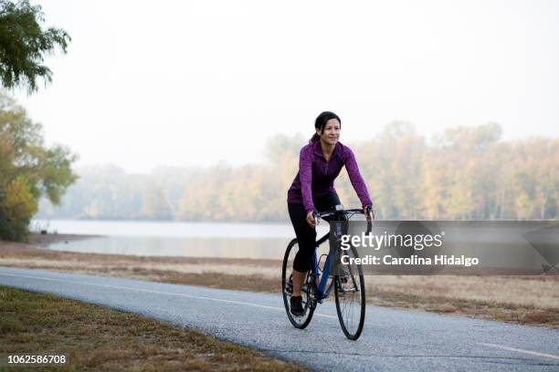 Latina Hispanic woman athlete riding a bicycle in park near lake