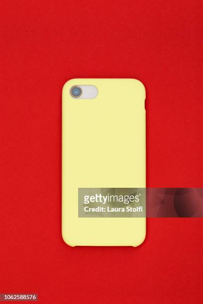 rear sight of smart phone with pale yellow cover against pop red background - coprire foto e immagini stock