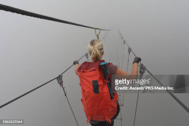 female hiker follows suspension bridge into fog - bridge fog stock pictures, royalty-free photos & images