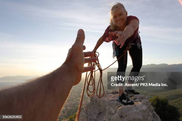 female rock climber extends a helping hand to teammate - part of a series foto e immagini stock
