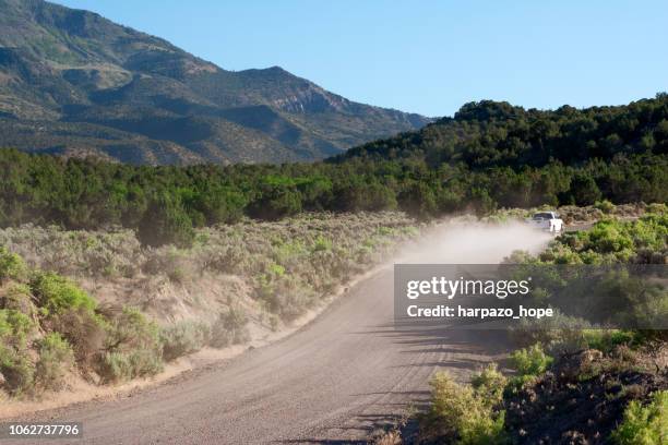 pick-up truck with dust cloud driving on a mountainous road in utah. - country road stock pictures, royalty-free photos & images