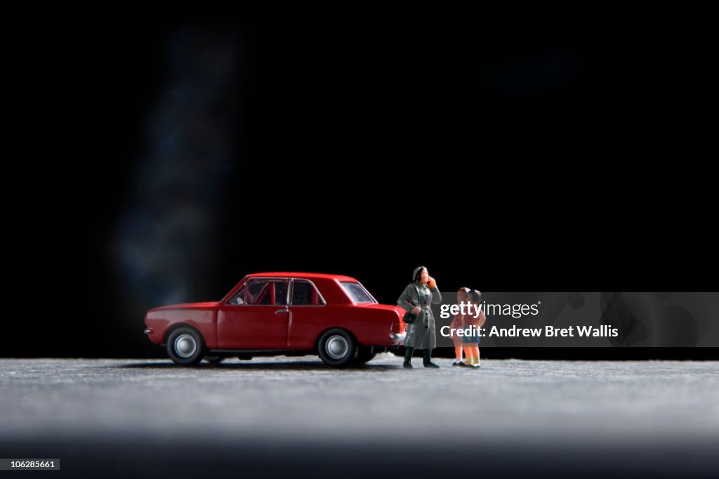 Model family standing near a broken down toy car