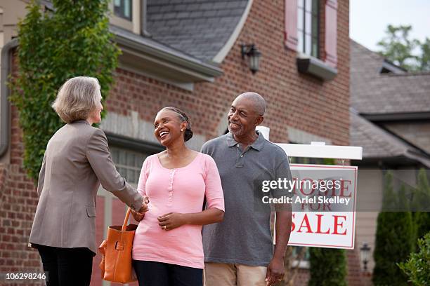 real estate agent shaking hands with smiling couple outside house for sale - baby boomer home stock pictures, royalty-free photos & images