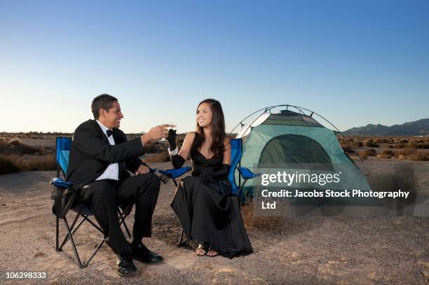 couple in formal attire toasting champagne glasses outside tent in desert - smoking photos et images de collection