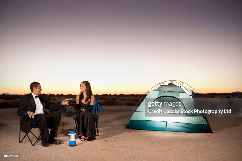 Couple in formal attire toasting champagne glasses outside tent in desert