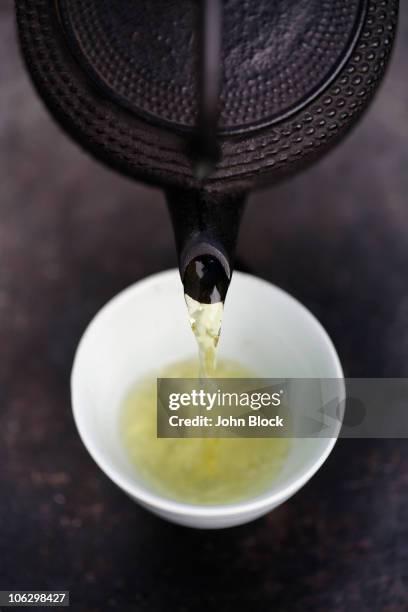 close up of japanese green tea being poured from teapot into cup - théière photos et images de collection