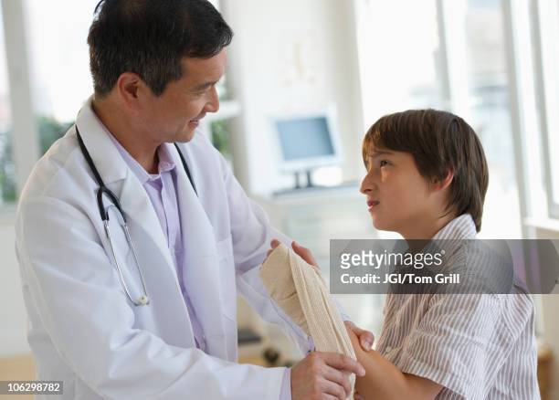 doctor wrapping boy's hand with bandage in examination room - boy broken arm stock pictures, royalty-free photos & images