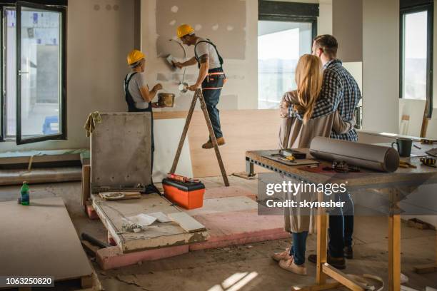 back view of embraced couple supervising works at their new apartment. - rebuilding stock pictures, royalty-free photos & images