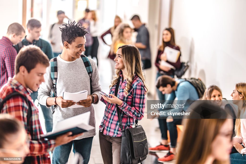 Happy teenage students talking in a hallway full of people.