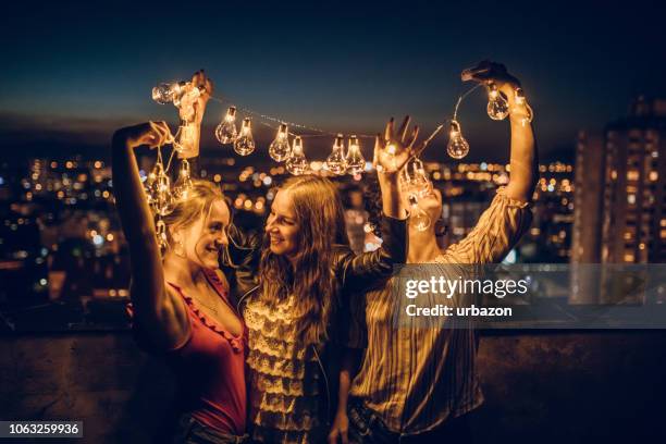 drie jonge vrouwen knuffelen op dak - summer lights stockfoto's en -beelden