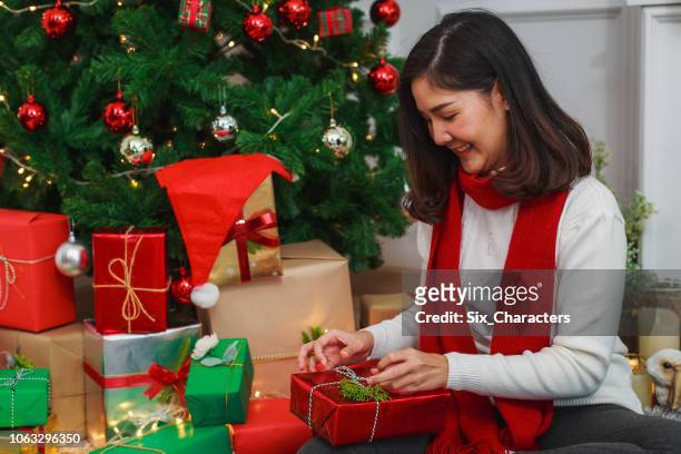 jeune femme asiatique assise sur le sol et pack emballage de cadeaux en face de l’arbre de noël sur le salon, les vacances de noël et les cadeaux concept jour de boxe - asian six pack photos et images de collection