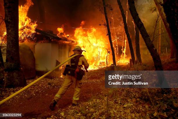 Cal Fire firefighter pulls a hose towards a burning home as the Camp Fire moves through the area on November 9, 2018 in Magalia, California. Fueled...