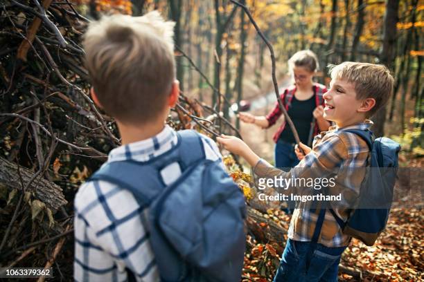 children building stick shelter in autumn forest - hut stock pictures, royalty-free photos & images