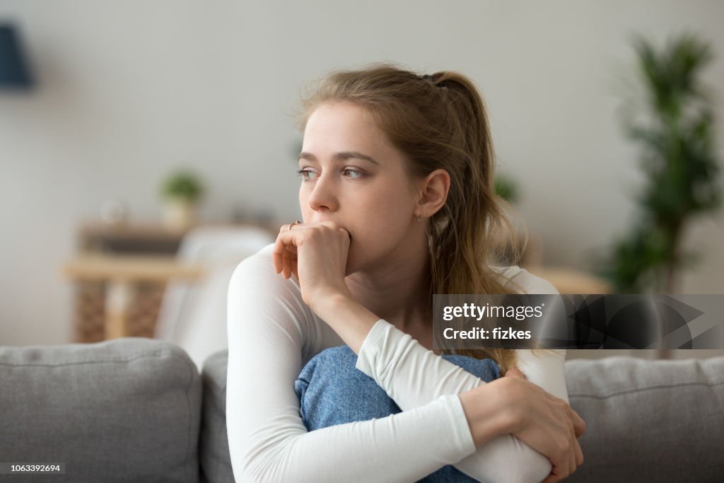 Sad woman sitting on couch alone at home