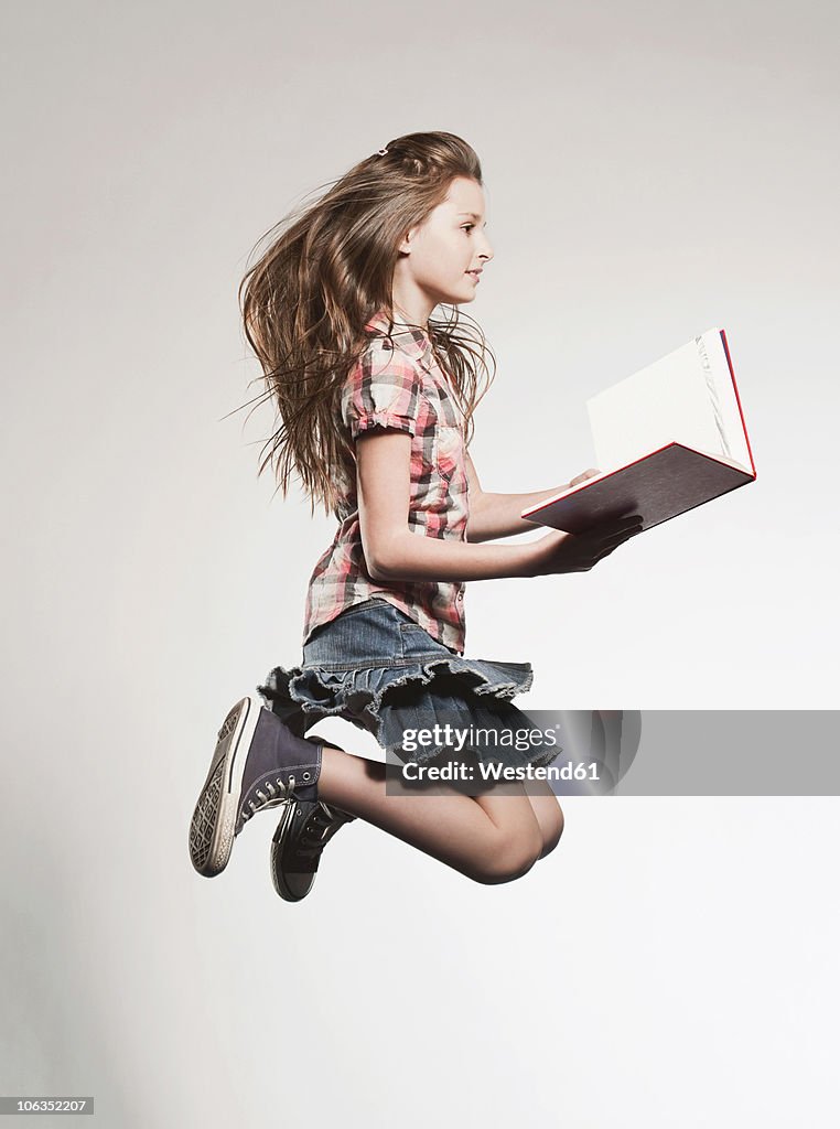 Girl (8-9) holding book and jumping, side view