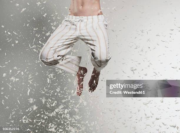 teenage boy (16-17) jumping in falling feathers, low section - falling feathers stock pictures, royalty-free photos & images
