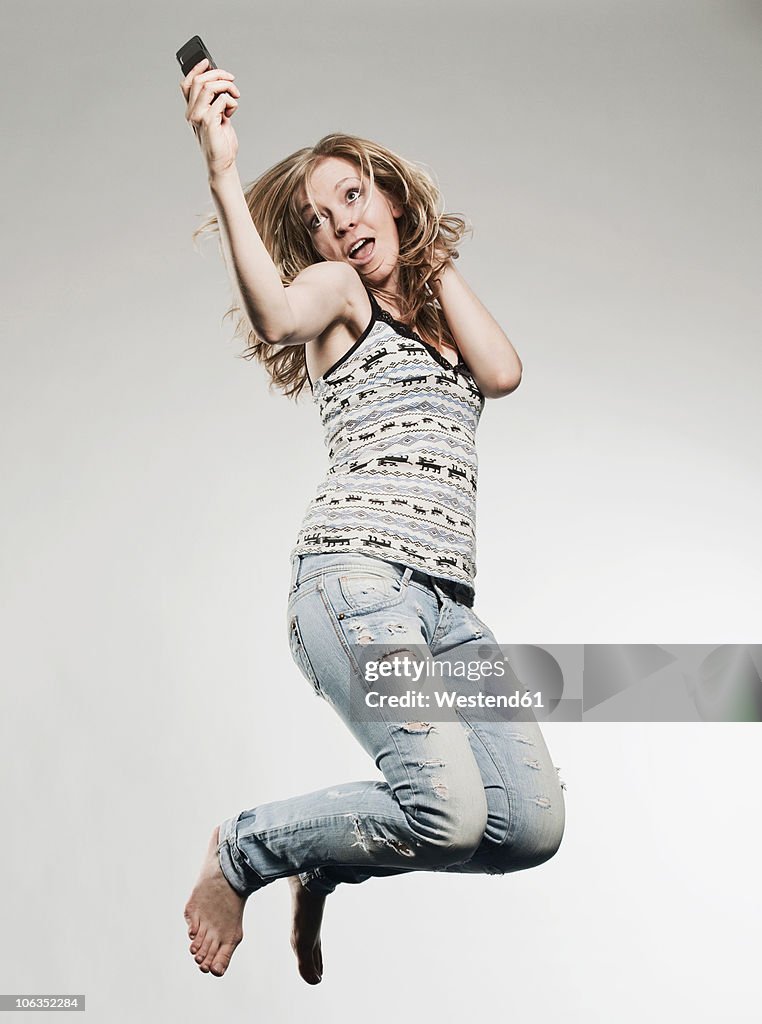 Woman holding mobile phone and jumping