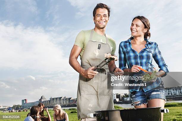 germany, cologne, man and woman barbecueing with friends in background - tongs stock-fotos und bilder