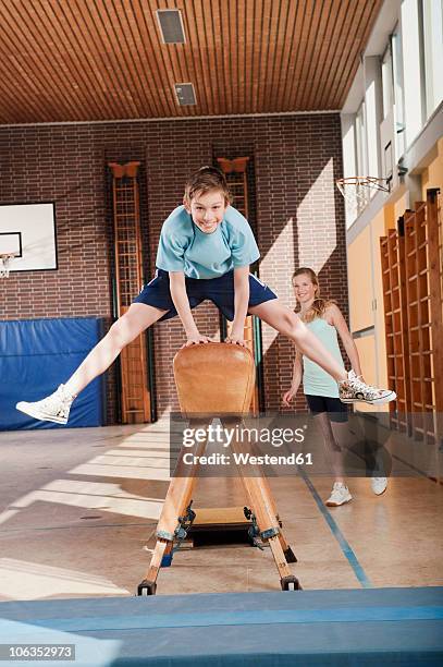 germany, emmering, boy (12-13) jumping with girl standing in background - gymnastics vault stock pictures, royalty-free photos & images