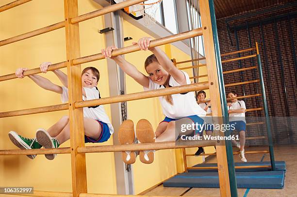 germany, emmering, girls (12-14) climbing wall bars with boys in background - gymnastics equipment stock pictures, royalty-free photos & images