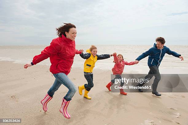 germany, st. peter-ording, north sea, family holding hands and running on beach - st peter ording stock pictures, royalty-free photos & images