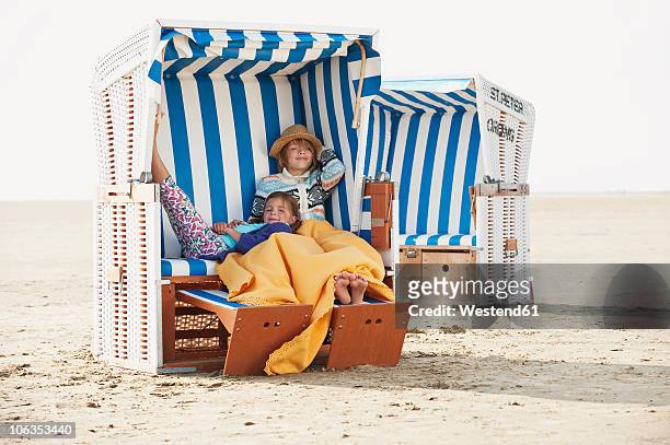 germany, st.peter-ording, north sea, children (6-9) resting on hooded beach chair - strandkorb stockfoto's en -beelden