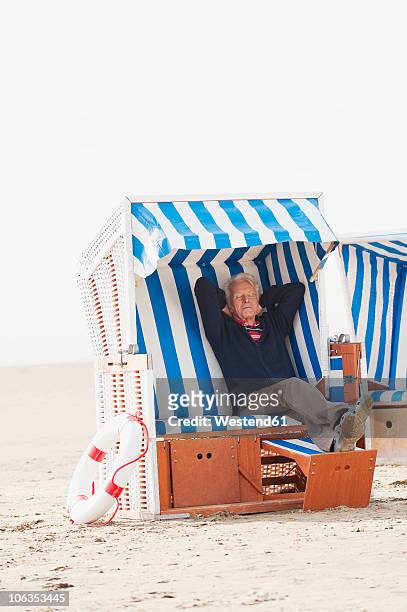 germany, st. peter-ording, north sea, senior man relaxing on hooded beach chair - beach shelter stock-fotos und bilder