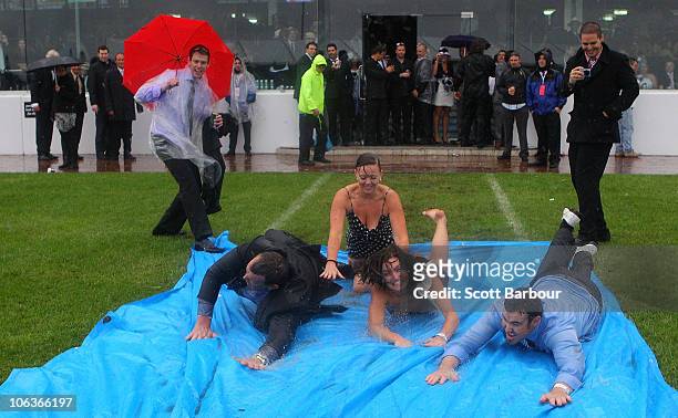 Race-goers slide along the ground in the rain during the AAMI Victoria Derby Day at Flemington Racecourse on October 30, 2010 in Melbourne, Australia.