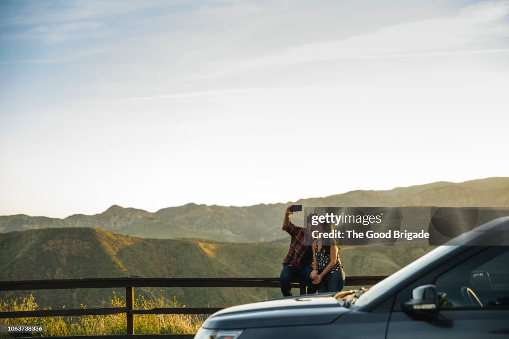 Couple taking selfie while sitting on fence in countryside