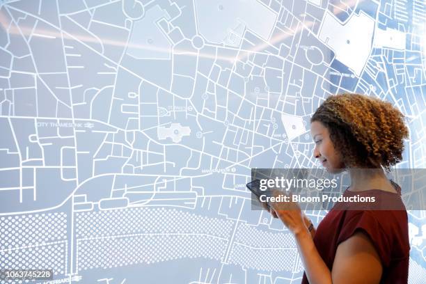 woman using a smartphone, next to a futuristic digitally generated display - globe navigational equipment stock-fotos und bilder