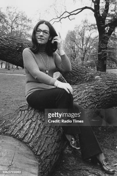 Portrait of singer Nana Mouskouri sitting on a tree trunk in a park, April 1974.