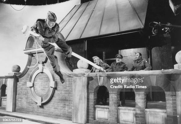 Actor Clive Dunn climbing a flag pole, watched by John Le Mesurier, Arthur Lowe and James Beck, in a scene from the episode 'Battle of the Giants!'...